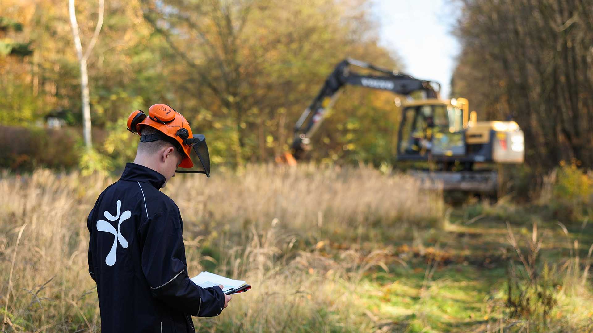 Mitarbeiter liest Arbeitsplan, Bagger im Hintergrund